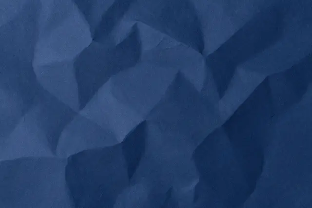 Full frame close-up of crumpled navy blue paper with soft highlights along folded ridges