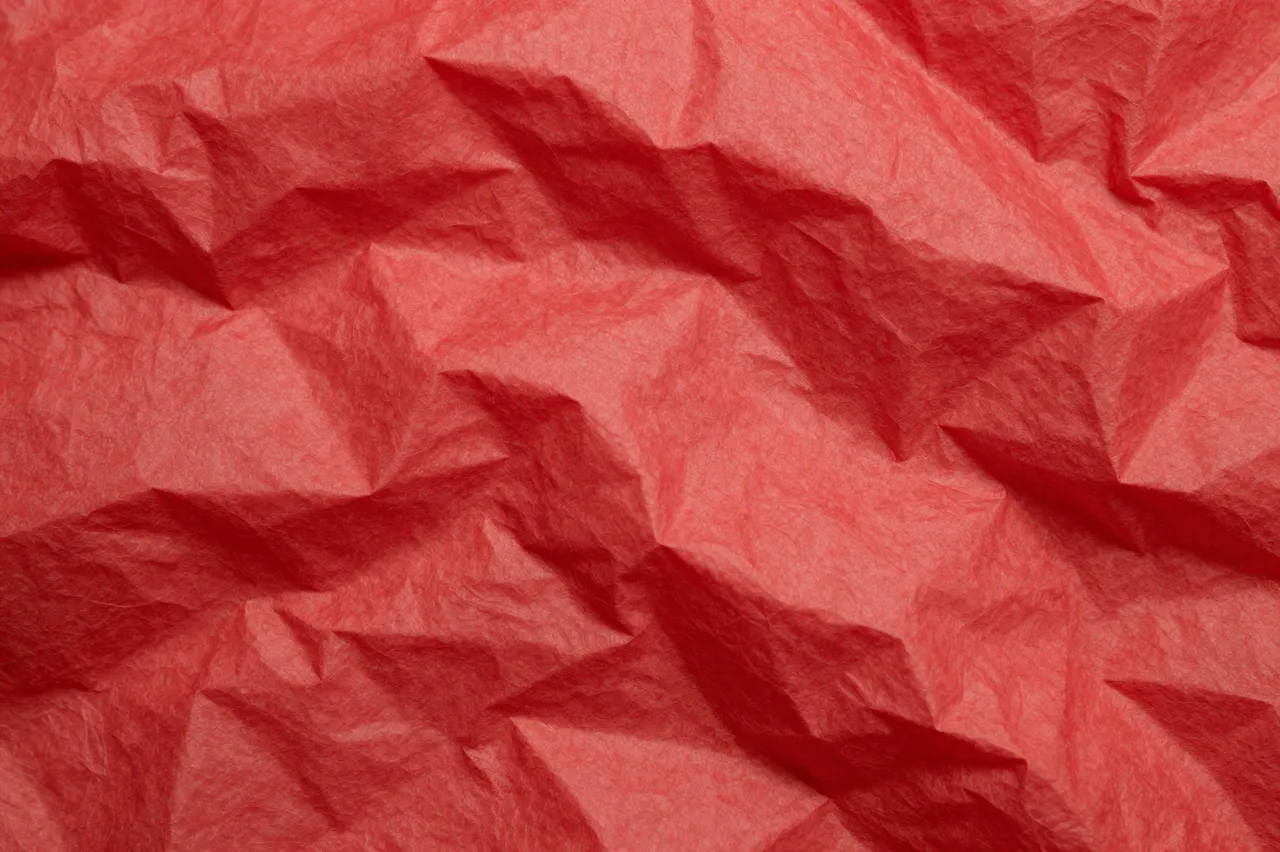 Close-up full frame of crumpled translucent red tissue paper with soft folded creases and gentle shadows