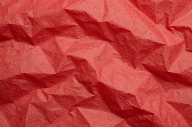 Close-up full frame of crumpled translucent red tissue paper with soft folded creases and gentle shadows