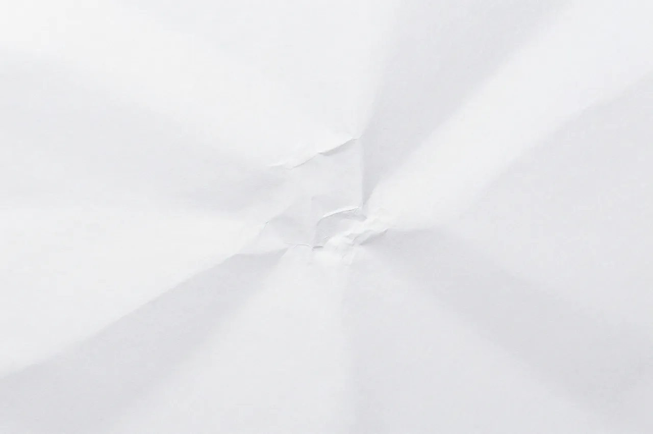 Close-up view of a crumpled plain white paper surface with soft fold shadows.
