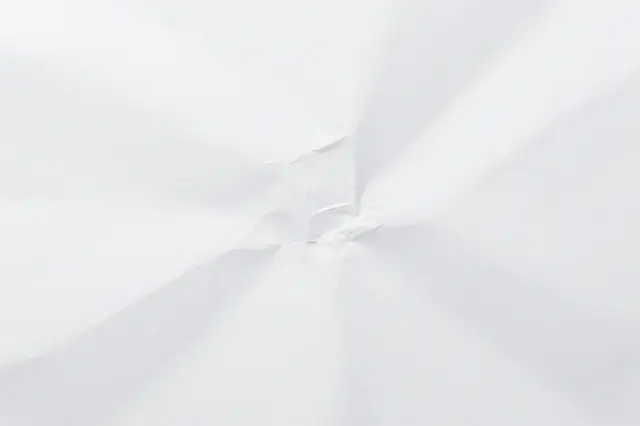 Close-up view of a crumpled plain white paper surface with soft fold shadows.