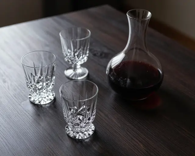 Cut crystal glasses and a red wine decanter rest on a dark wood table in low moody light
