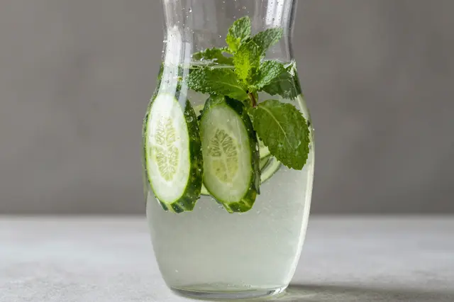 Glass pitcher of cucumber and mint infused water resting on a light gray countertop