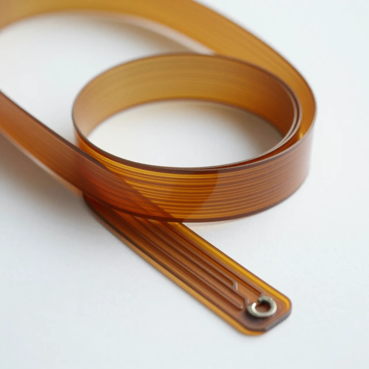 A curled flexible amber ribbon circuit rests flat on a clean white surface under soft light