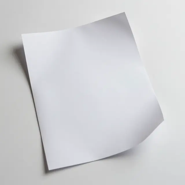A plain white sheet of paper with a soft corner curl rests on a flat white surface casting a gentle shadow.