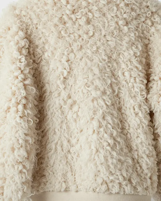 Full frame close-up of soft curly cream shearling fleece fabric with springy tufts