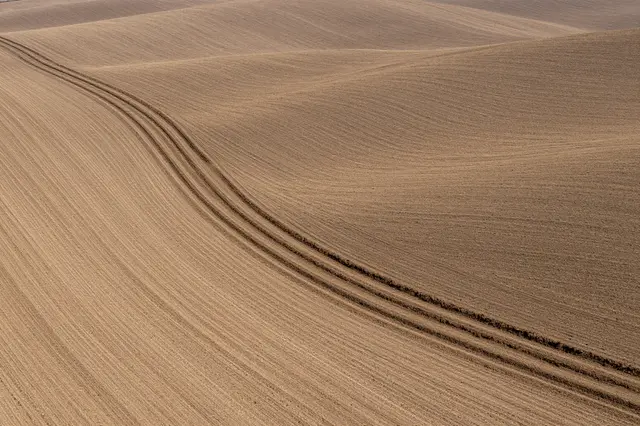 Aerial view of smooth curved contour plowing lines across rolling brown farm hills in early spring
