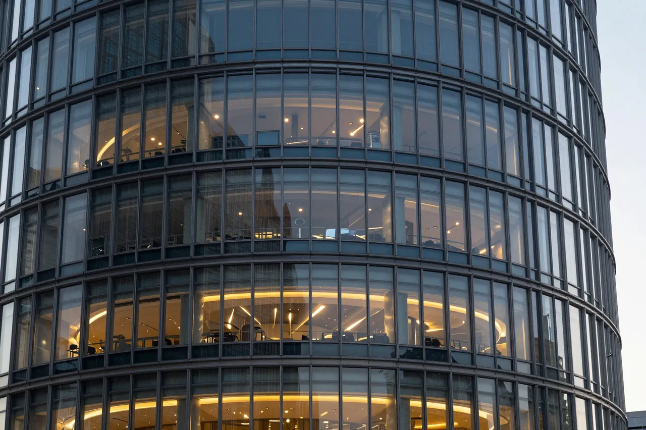 Close-up view of a curved modern glass skyscraper facade with warm interior lighting at dusk