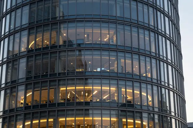 Close-up view of a curved modern glass skyscraper facade with warm interior lighting at dusk