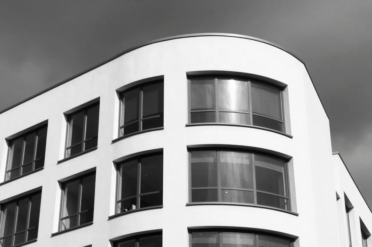 Black and white low-angle shot of a curved white modernist building under a dark overcast stormy sky