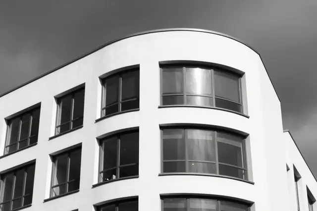 Black and white low-angle shot of a curved white modernist building under a dark overcast stormy sky