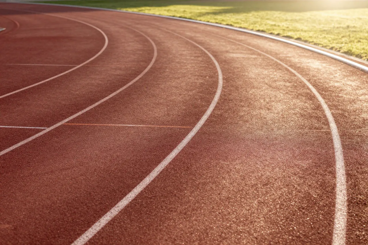 Low angle view of an empty curved running track under warm golden sunrise light next to grass