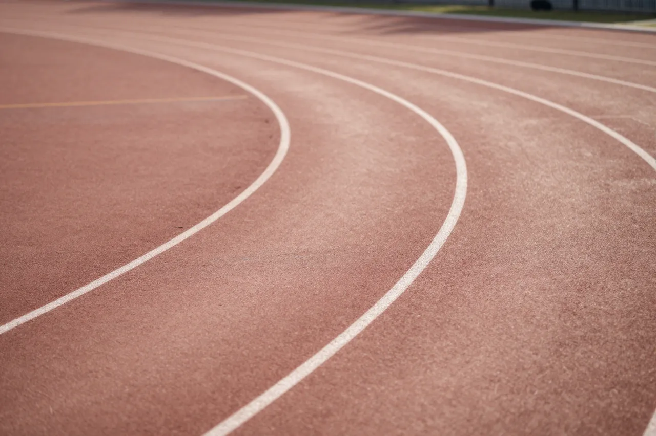 Empty curved red running track with white lane markings lit by soft natural light