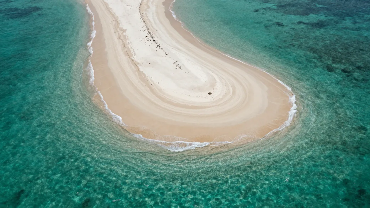 Aerial view of a sweeping curved sandbar surrounded by clear turquoise ocean shallows