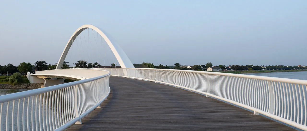 View along a curving modern white pedestrian bridge over a calm river at dusk, with no people present