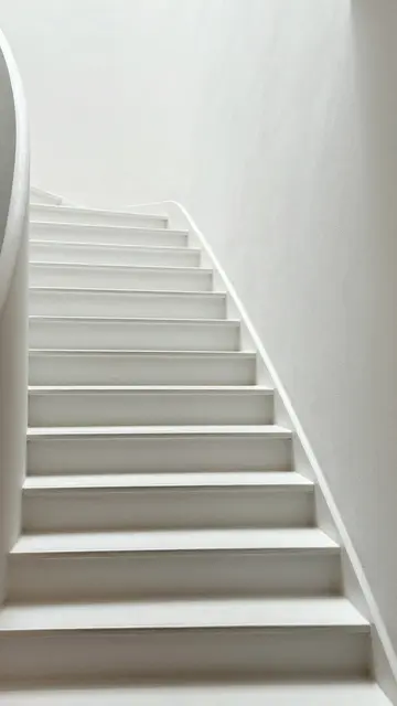 Minimalist white curved staircase ascends alongside smooth plaster walls in soft even light