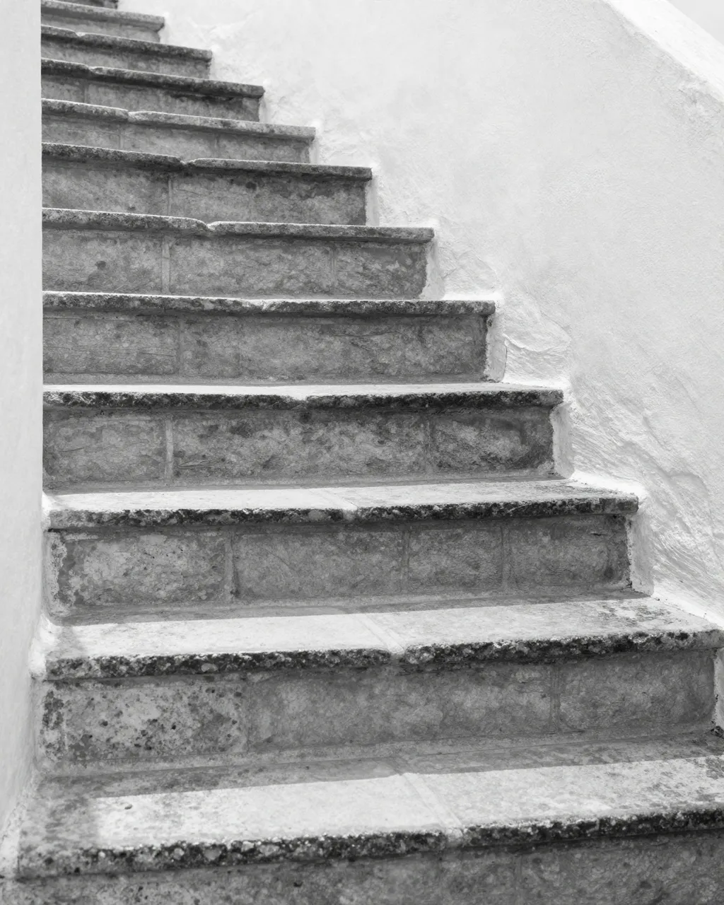 Black and white view of sunlit worn stone steps curving upward between whitewashed plaster walls