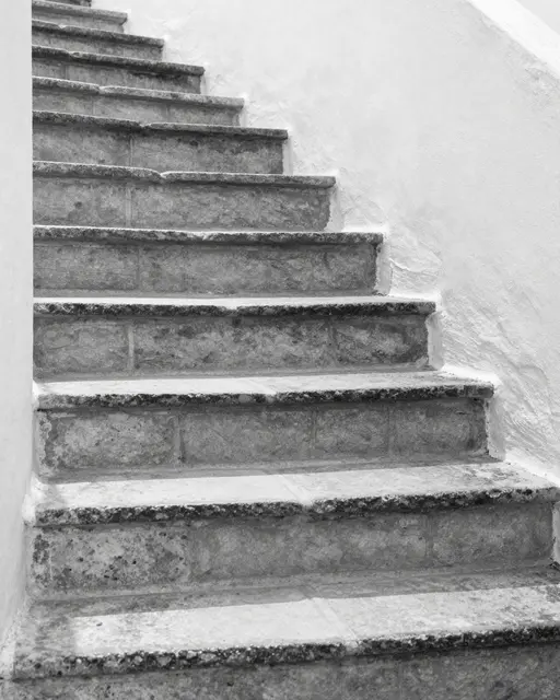 Black and white view of sunlit worn stone steps curving upward between whitewashed plaster walls