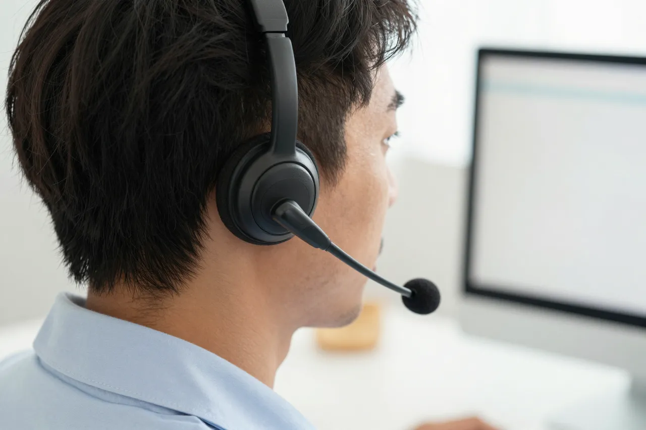 Side profile close-up of a customer service agent wearing a headset looking toward a blurred computer monitor at an office
