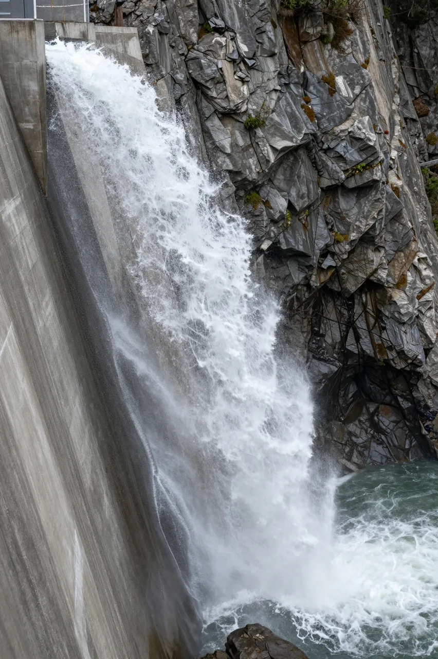 Turbulent white water erupts from a concrete dam spillway into a rocky gorge below