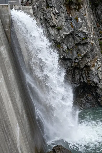 Turbulent white water erupts from a concrete dam spillway into a rocky gorge below
