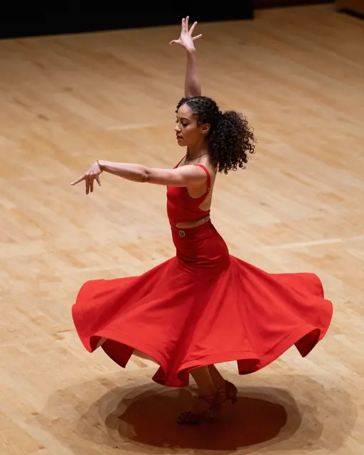 Mixed-race woman dancing alone on a wooden dance floor with her red skirt swirling mid-movement