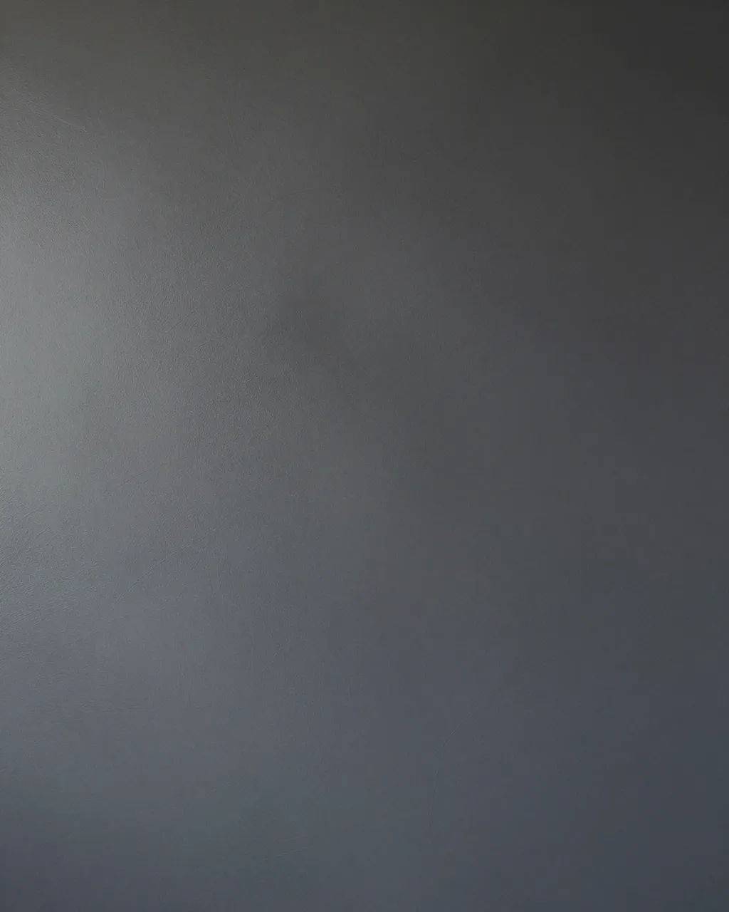 Full frame close-up of a soft mottled deep charcoal limewash wall surface with subtle brush strokes