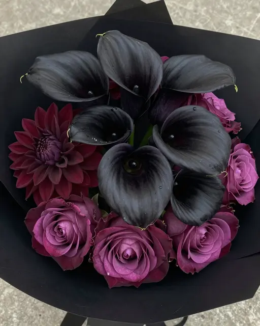 A moody bouquet of black calla lilies, burgundy dahlias and plum roses wrapped in black paper.