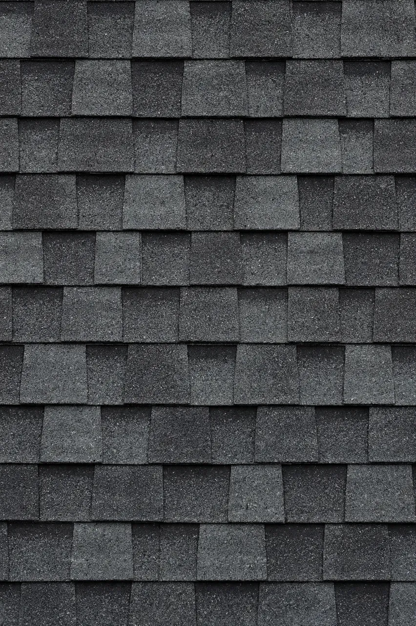 Full frame close-up of overlapping staggered dark gray asphalt roof shingles with a gritty granular surface