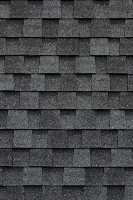 Full frame close-up of overlapping staggered dark gray asphalt roof shingles with a gritty granular surface