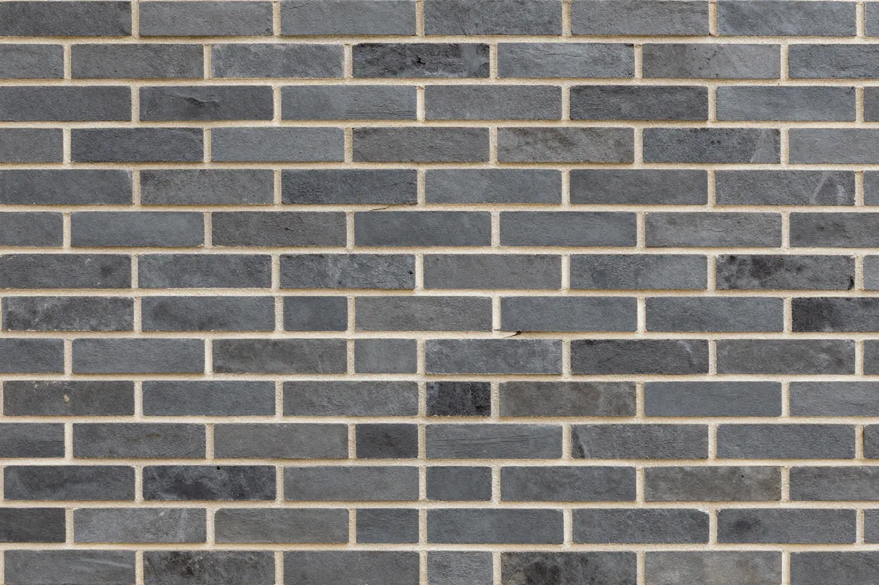 Full frame view of a dark gray brick wall with light pale mortar lines in running bond pattern