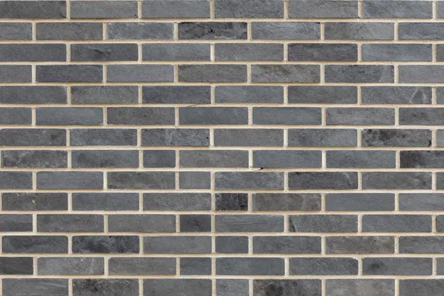 Full frame view of a dark gray brick wall with light pale mortar lines in running bond pattern