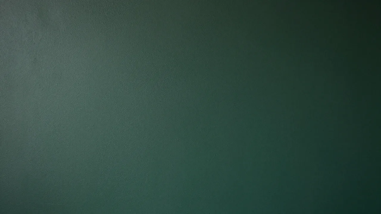 Full frame view of a textured forest green plaster wall with subtle lighting gradient
