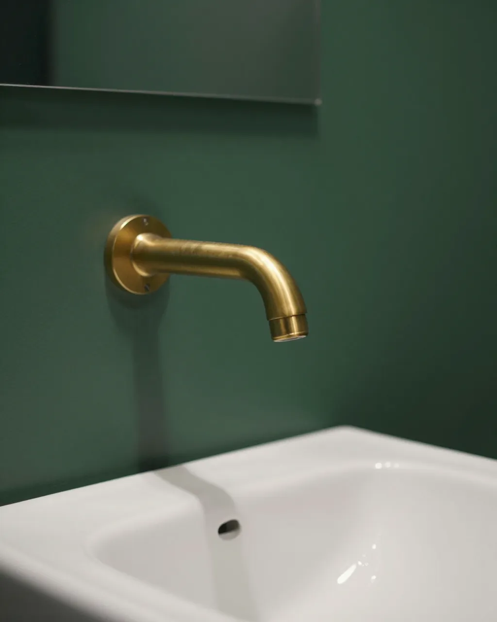 Brass wall-mounted faucet above a white sink against deep green bathroom walls