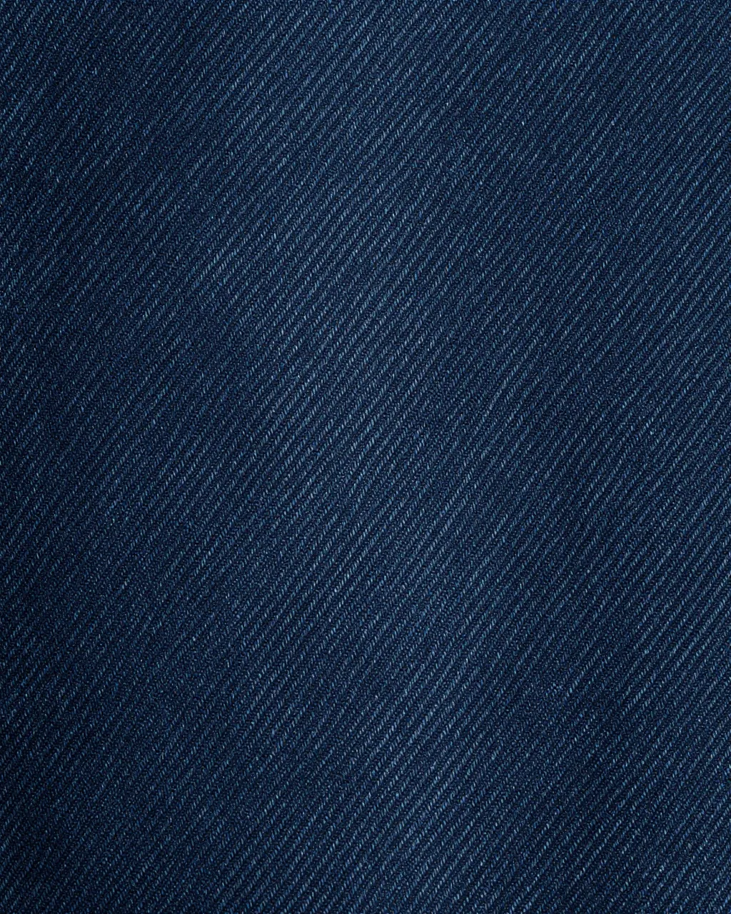 Close-up macro shot of dark indigo raw denim showing a fine diagonal twill weave pattern
