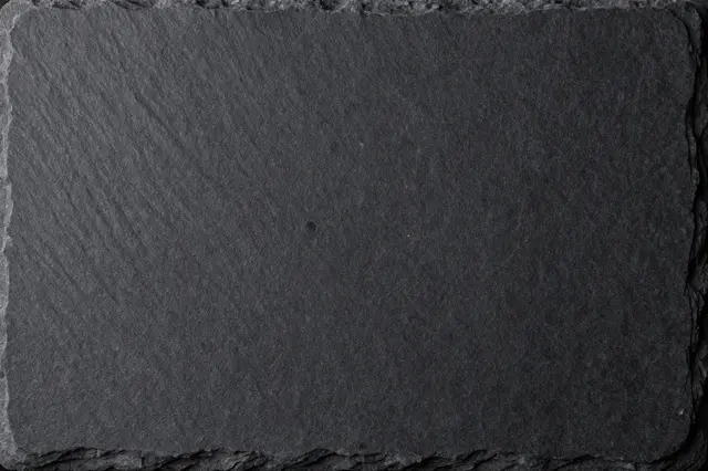Close up top view of a rough rectangular black slate stone surface with chipped natural edges