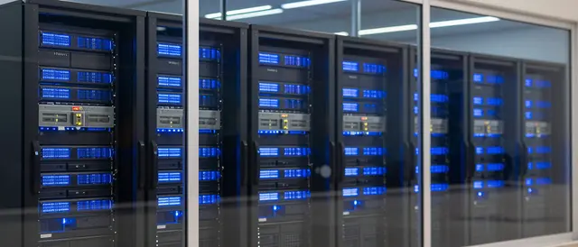 Rows of glowing blue server racks are visible through a glass partition in a data center.