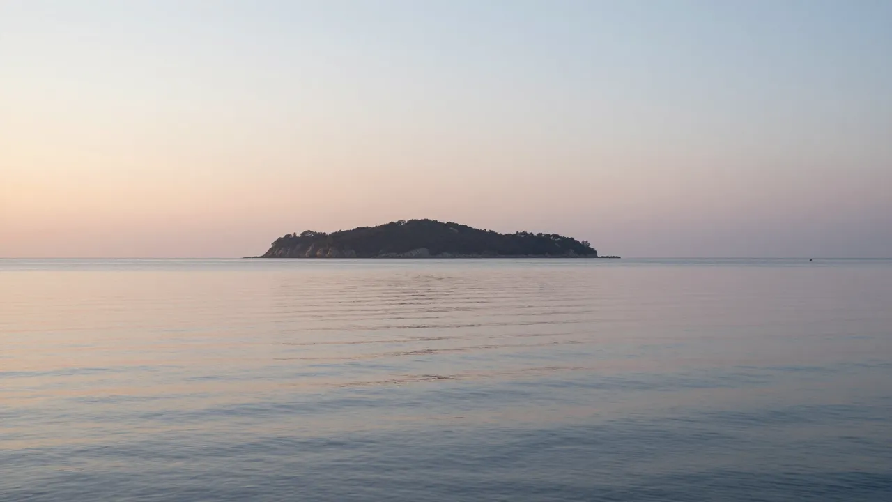 Pastel dawn light falls over a calm glassy sea with a forested low island on the horizon