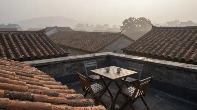 Wooden rooftop table with two cups overlooks misty old clay tile roofs at early dawn