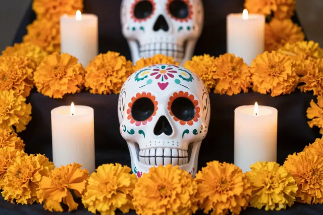 Decorated sugar skulls, lit candles, and bright orange marigolds arranged on a dark Day of the Dead altar.