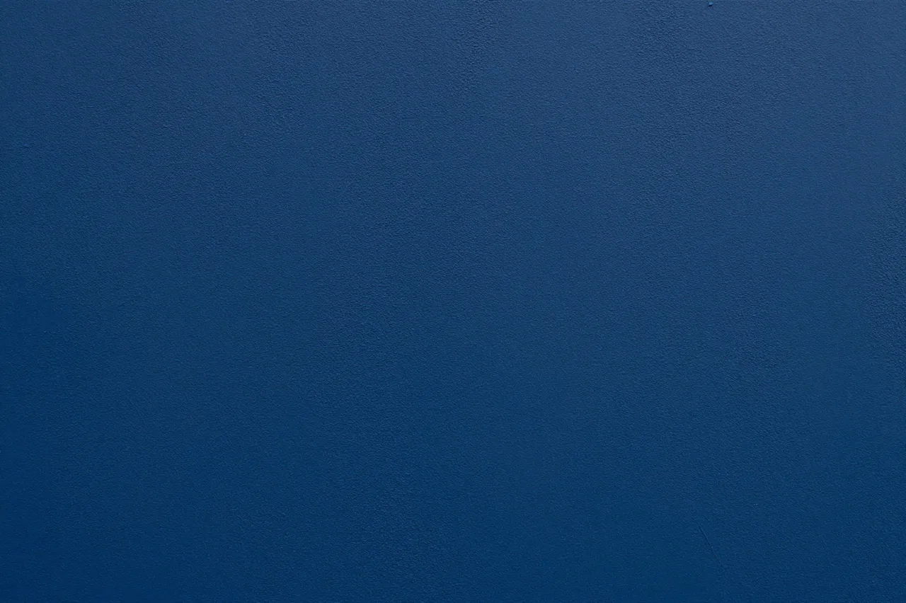 Full frame close-up of a rough deep blue painted stucco wall with soft subtle lighting