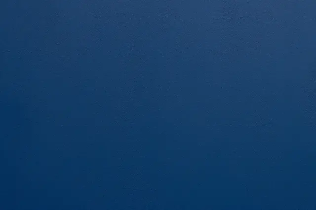 Full frame close-up of a rough deep blue painted stucco wall with soft subtle lighting