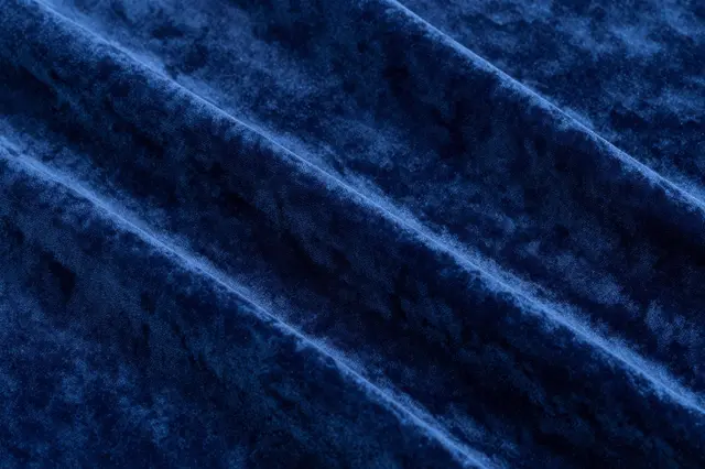 Close up of folded deep blue velvet fabric with soft diagonal ripples and plush texture