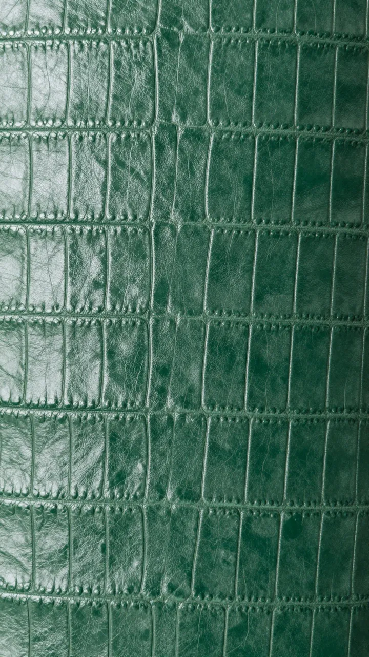 Full frame close-up of embossed deep forest green croc-effect leather with a soft subtle sheen