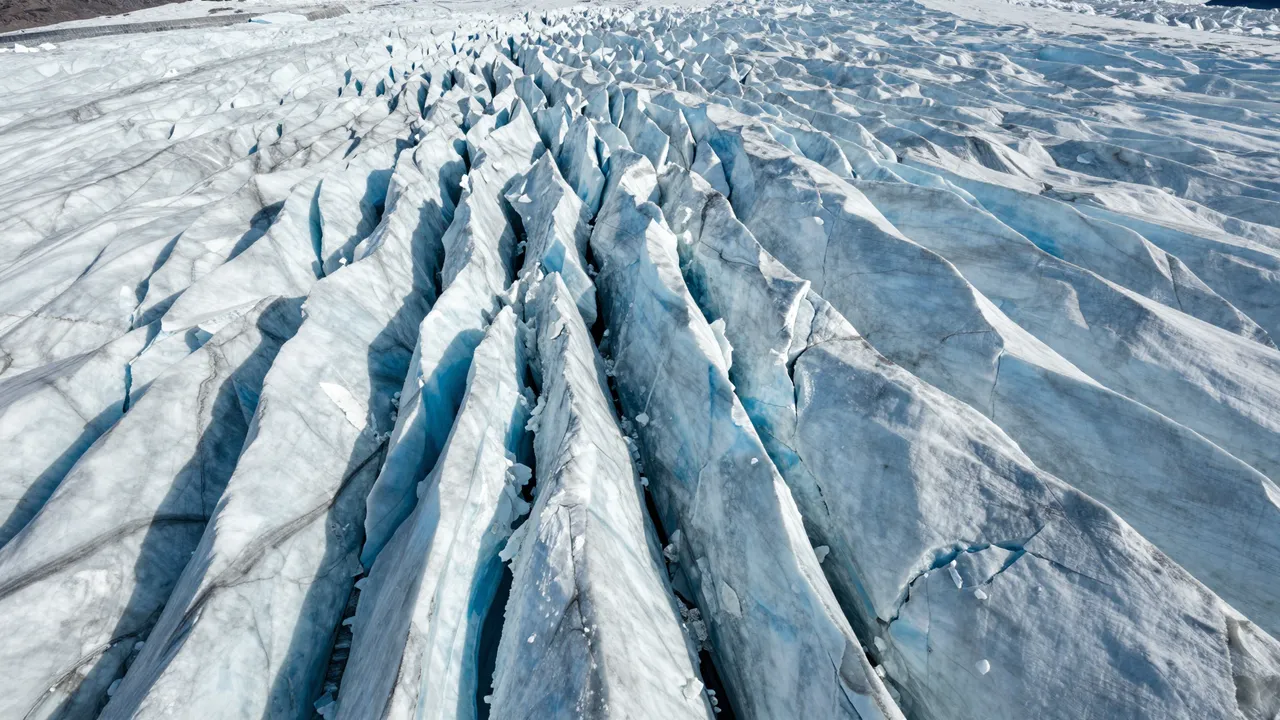 Aerial perspective of a textured glacier surface filled with deep bright blue ice crevasses