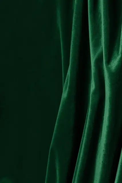 Tall background of deep green velvet fabric with soft sheen on the right and empty space on the left