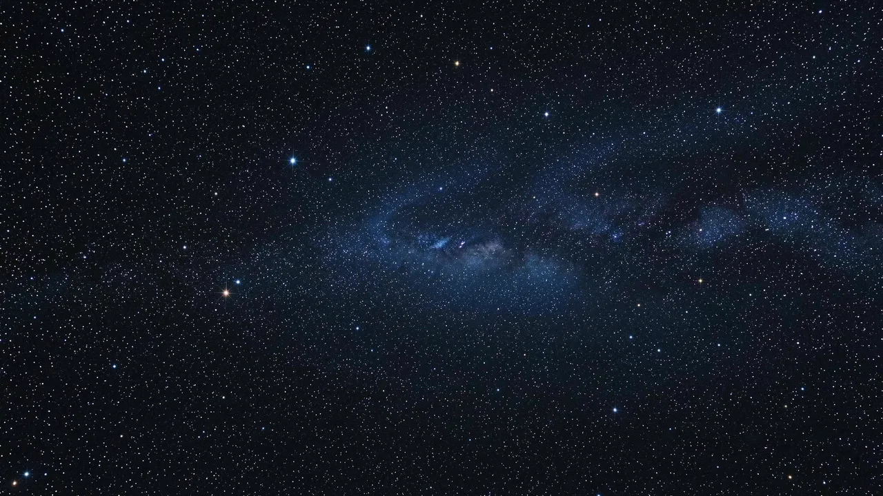 Dense starfield with a faint distant blue nebula stretches across dark cosmic space