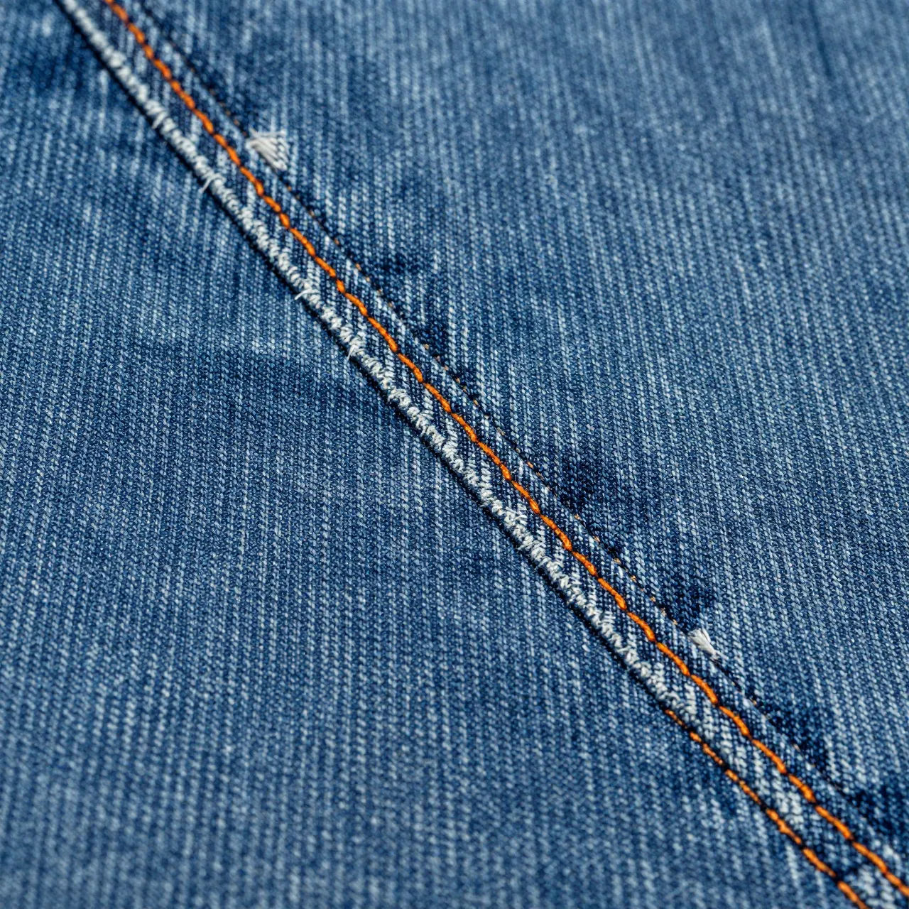 Close-up view of blue denim fabric with contrasting orange and white topstitching along a seam