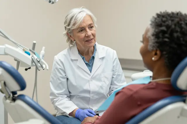 Senior female dentist speaks gently to an older woman seated in a dental office chair before a checkup