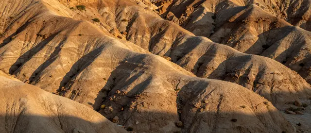 Eroded desert buttes are lit by warm golden sunset with long angular shadows across slopes
